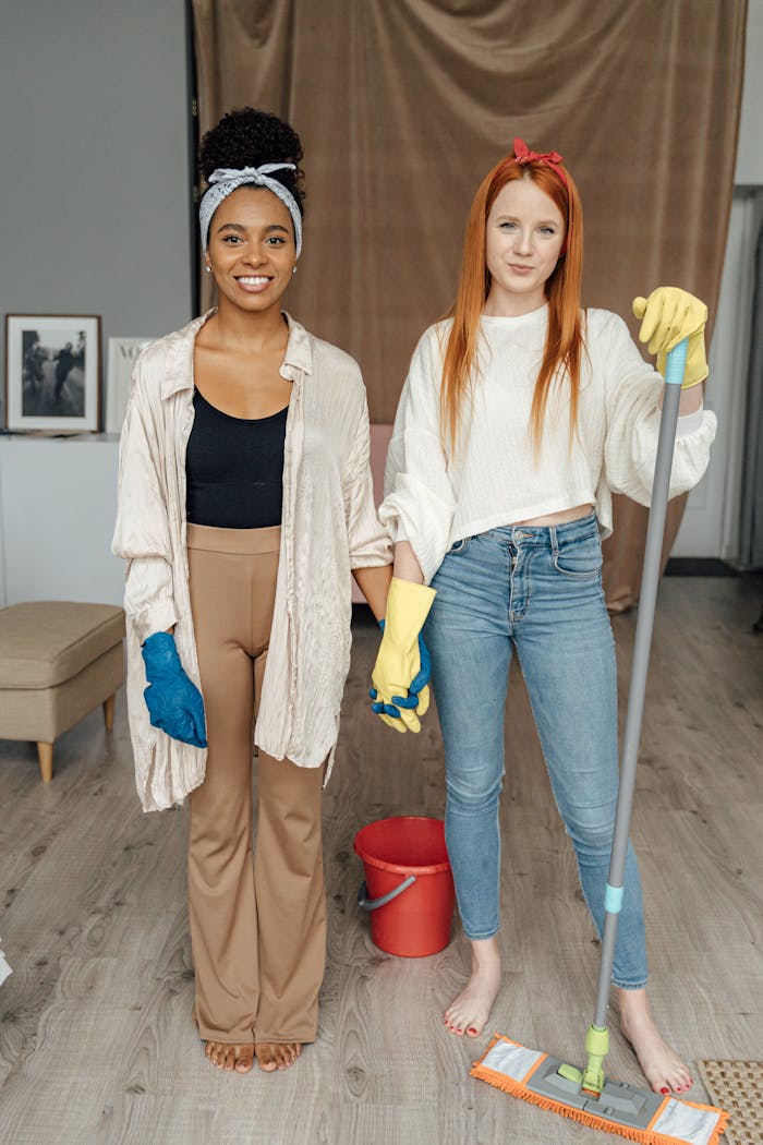 services-02 Two women smiling and holding hands while cleaning indoors, symbolizing teamwork.